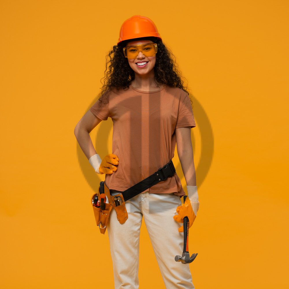 3415 sarı arkaplan önünde duran turuncu baretli işçi kadın gülümseyen çalışan kız
